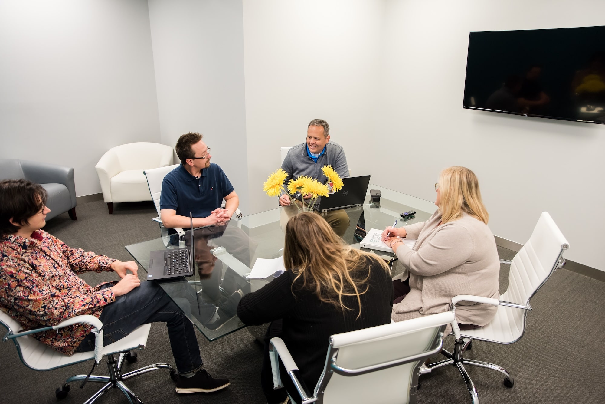 Five people meeting at the glass office table with white chairs.