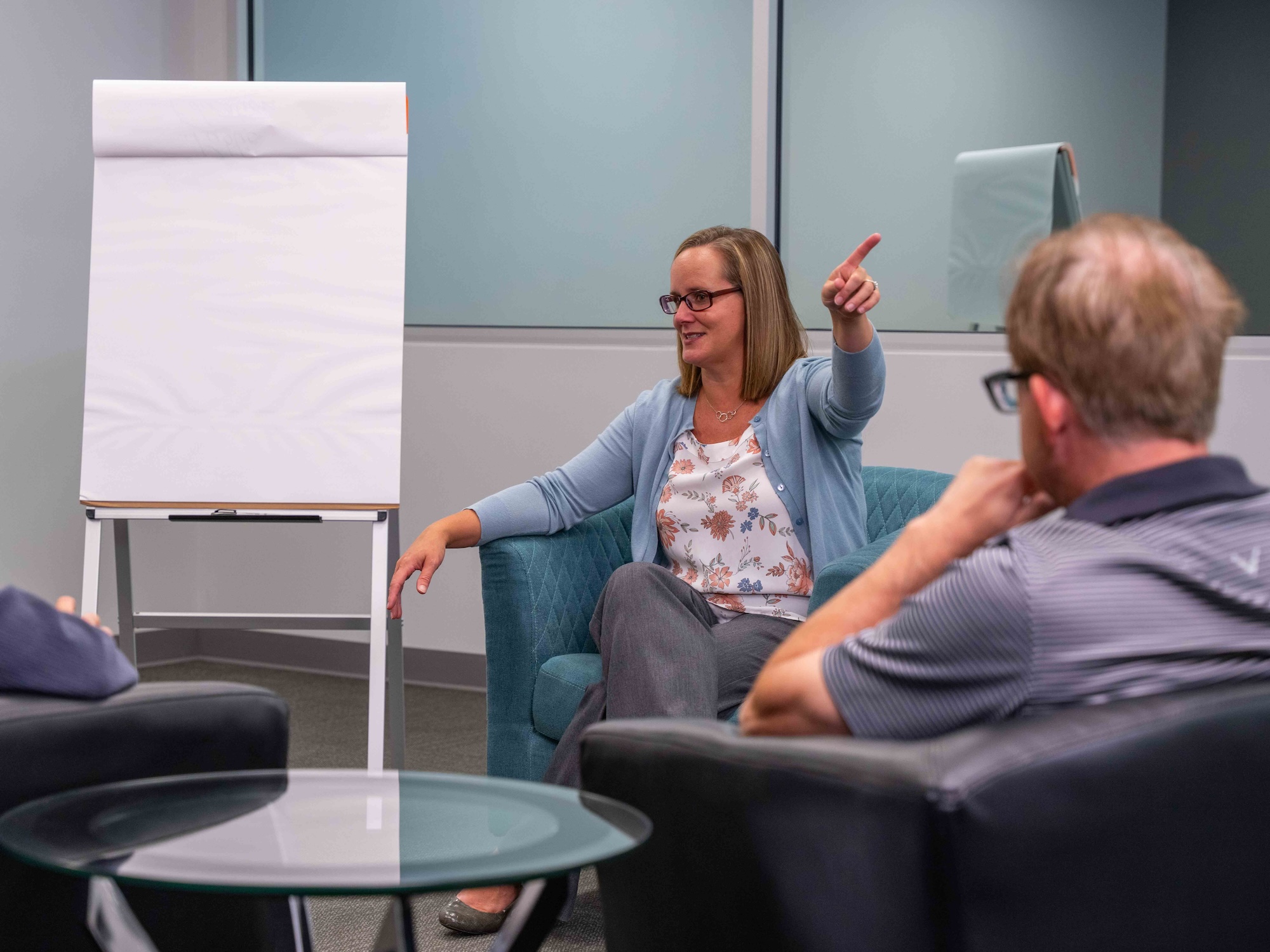 Facilitator leading a relaxed small-group discussion in a meeting space with comfortable seating and a blank flip chart.