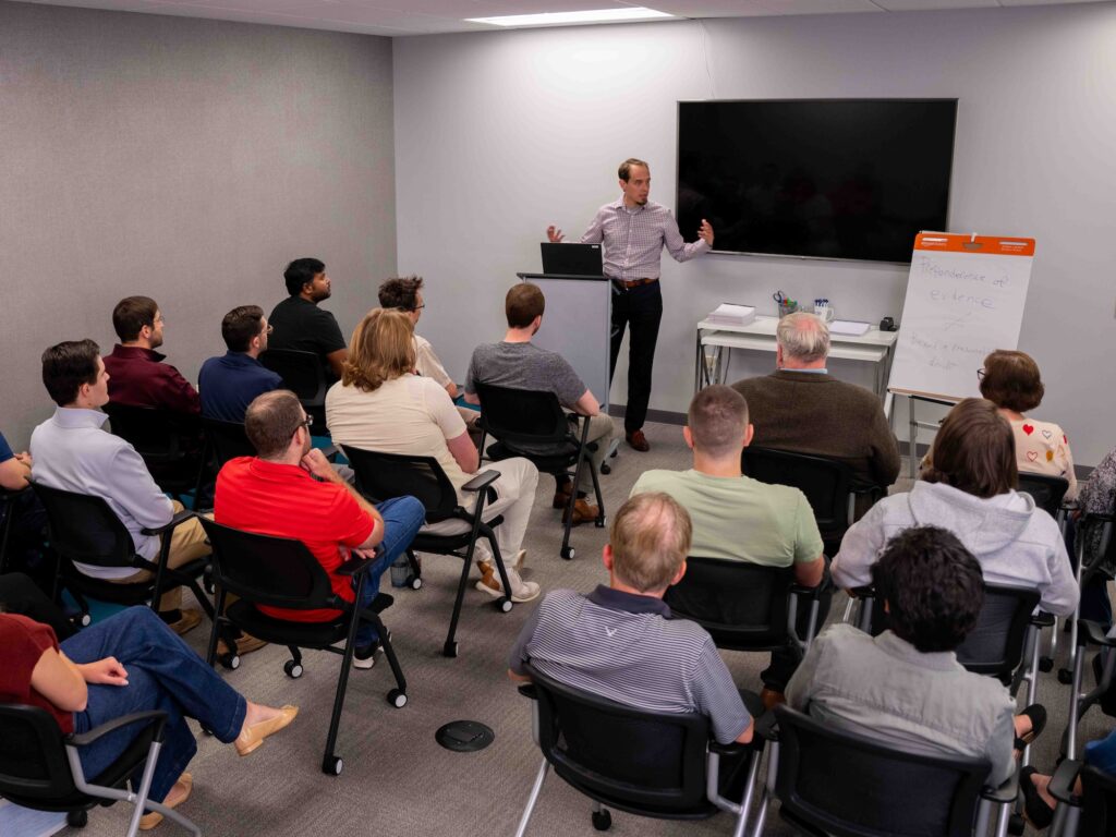 Presenter leading a focus group session at Beyond the Table Research, speaking to a full room of participants and explaining key concepts with a whiteboard and large screen at the front of the room.
