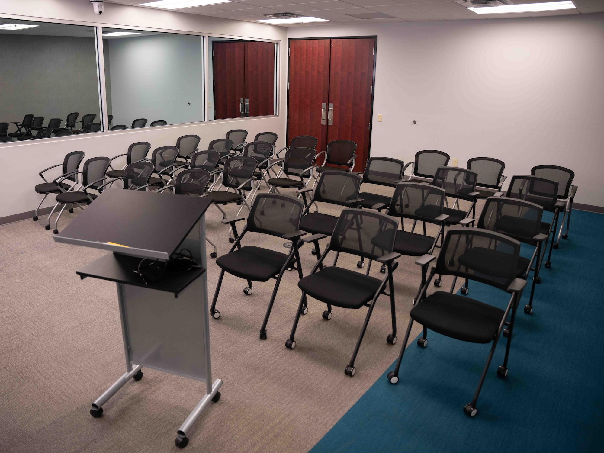 Modern conference room setup with rows of chairs, a podium, large display screen, and observation window at Beyond the Table Research, ready for a presentation or focus group session.